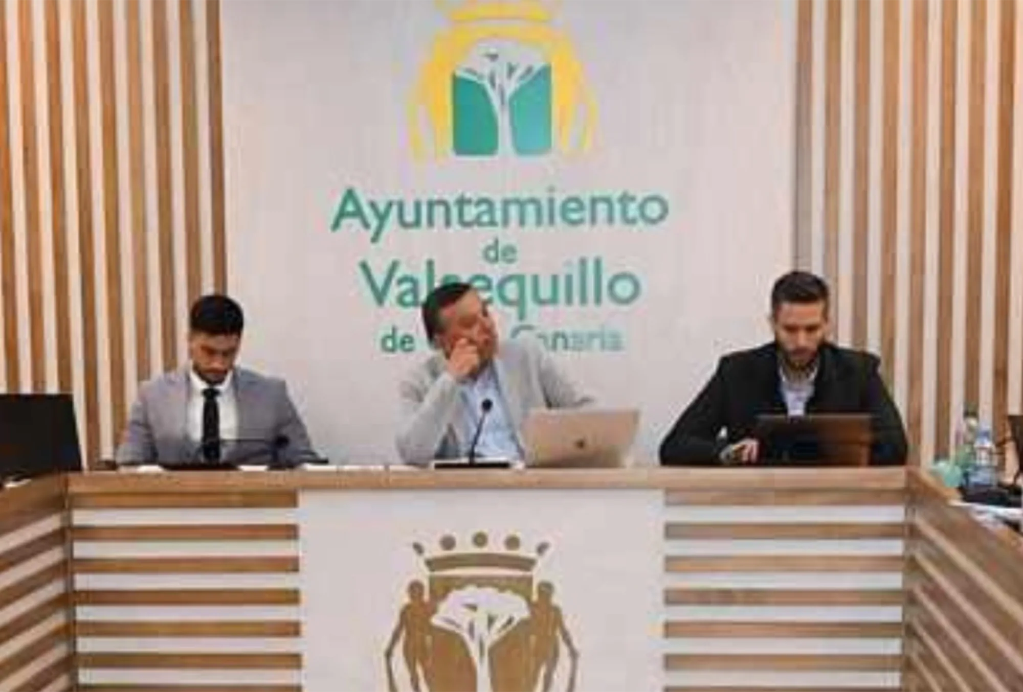 Tres personas sentadas a la mesa del salón de plenos del Ayuntamiento de Valsequillo, bajo el escudo municipal.